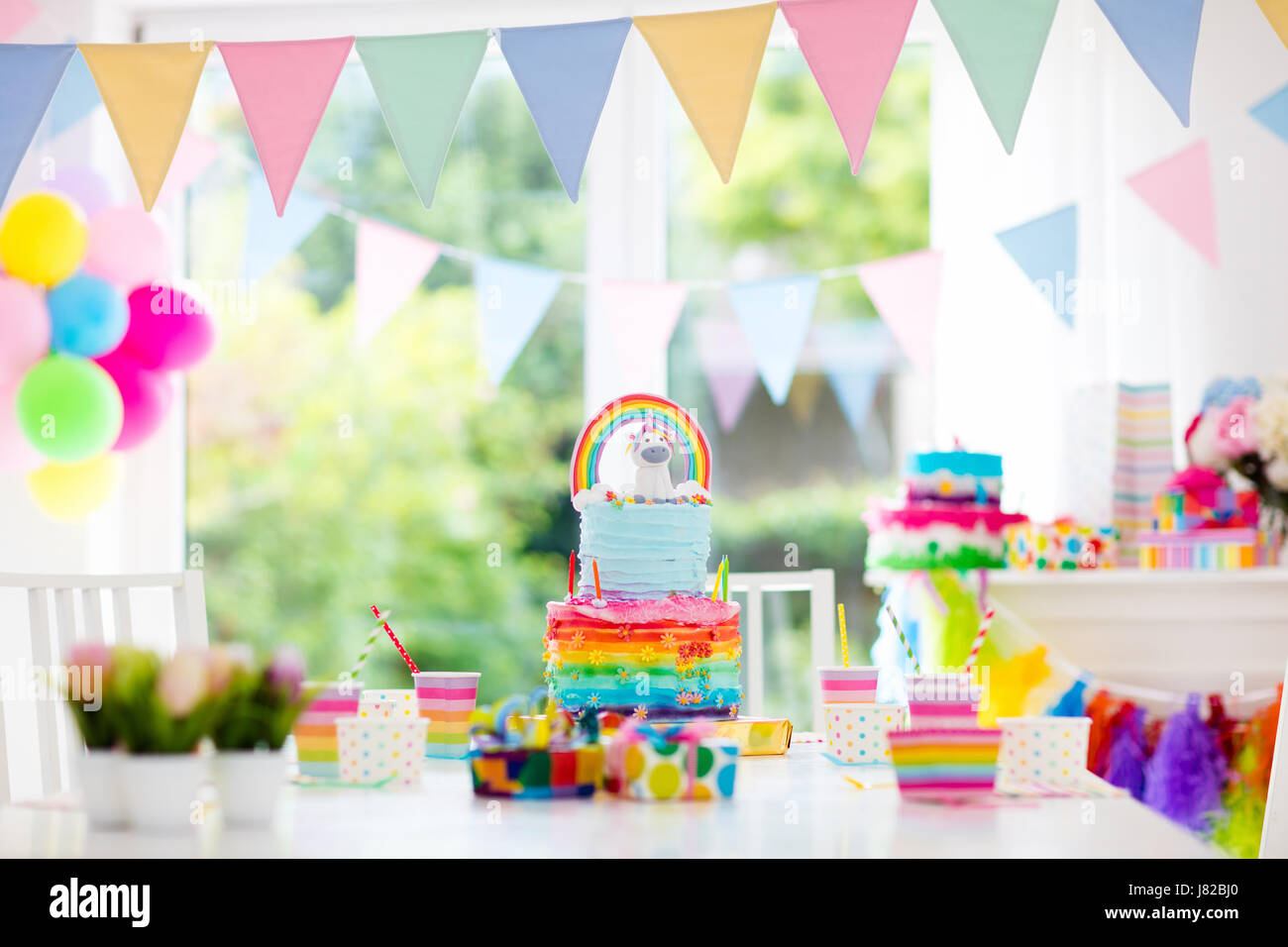 Kids birthday party decoration and cake. Decorated table for child birthday celebration. Rainbow unicorn cake for little girl. Room with festive ballo Stock Photo