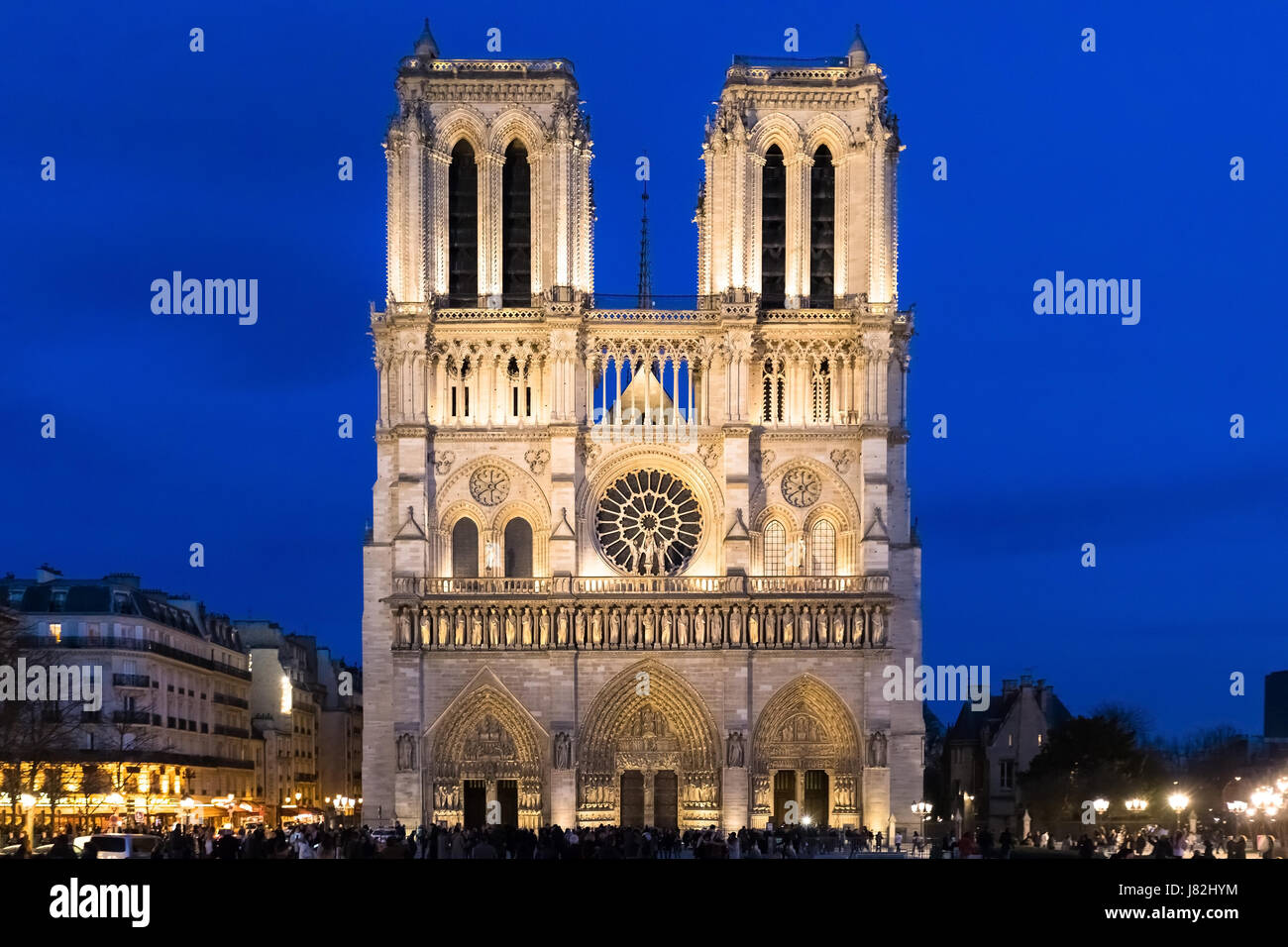 Main facade of Notre-Dame de Paris Cathedral at dusk with illuminations and blue sky, famous landmark of France, perspective correction Stock Photo