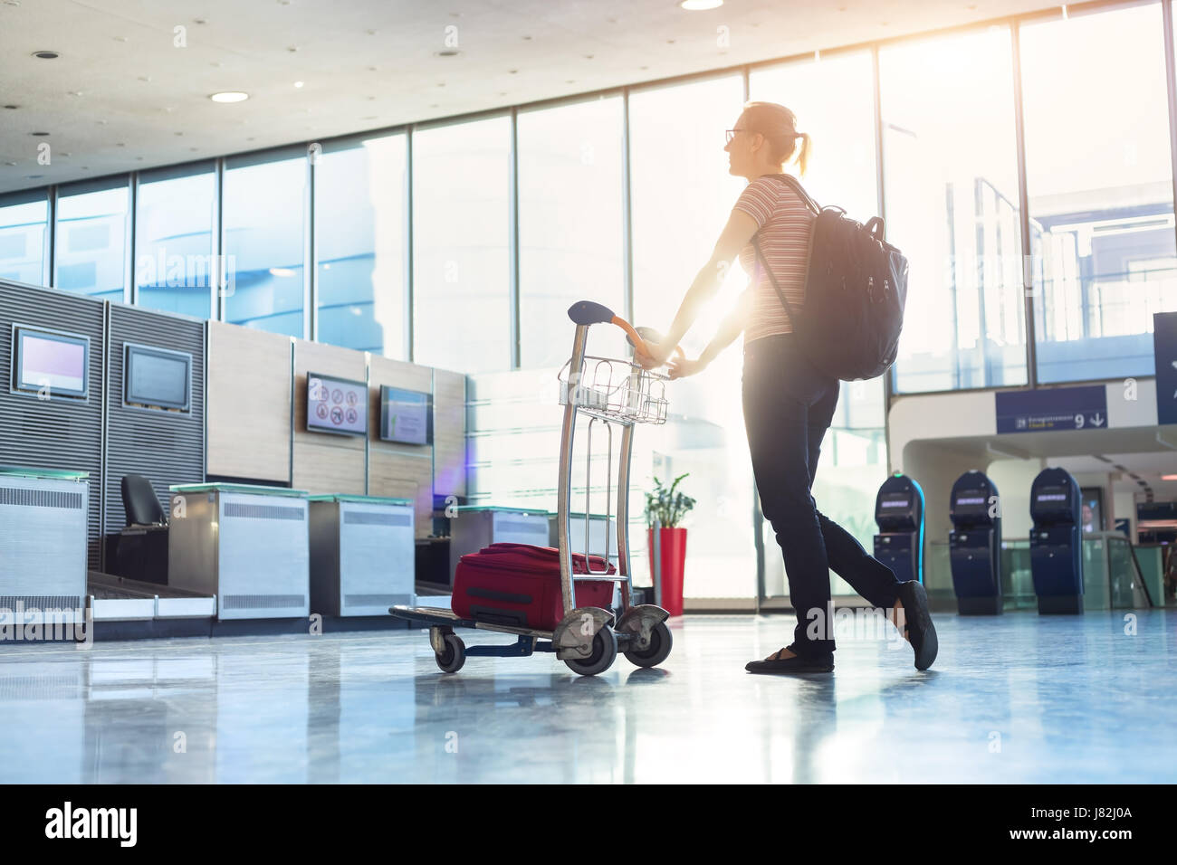 Woman walking with a luggage trolley to a airline check-in counter in a modern airport before an international flight Stock Photo