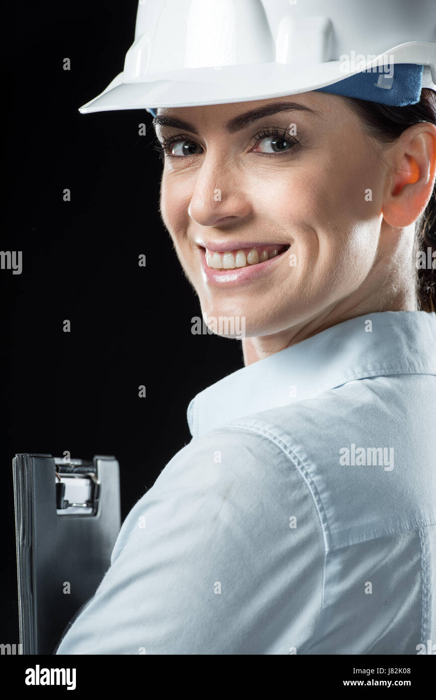 Female architect in helmet holding folder and smiling at camera Stock