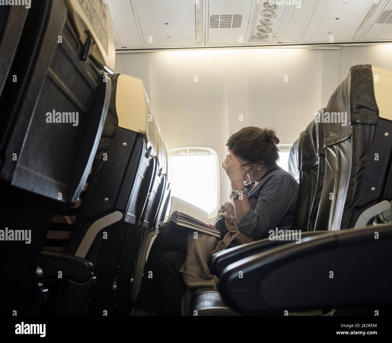 Ryanair flight: mature woman reading book in window seat. Stock Photo