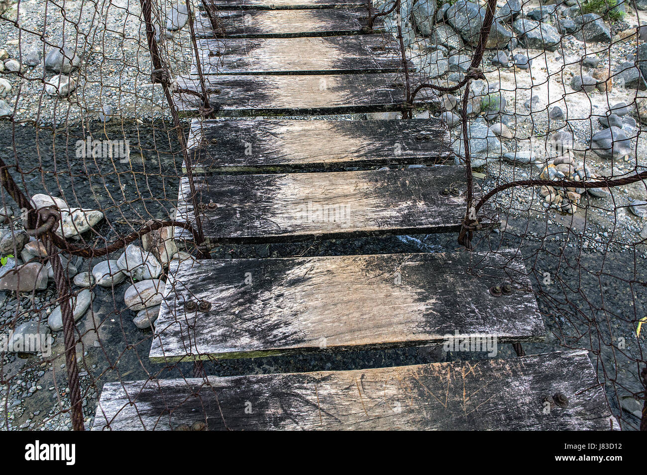 Well-worn wooden rungs of a cable and fence wire suspension bridge over a small river in northern Luzon Island, Philppines. Stock Photo