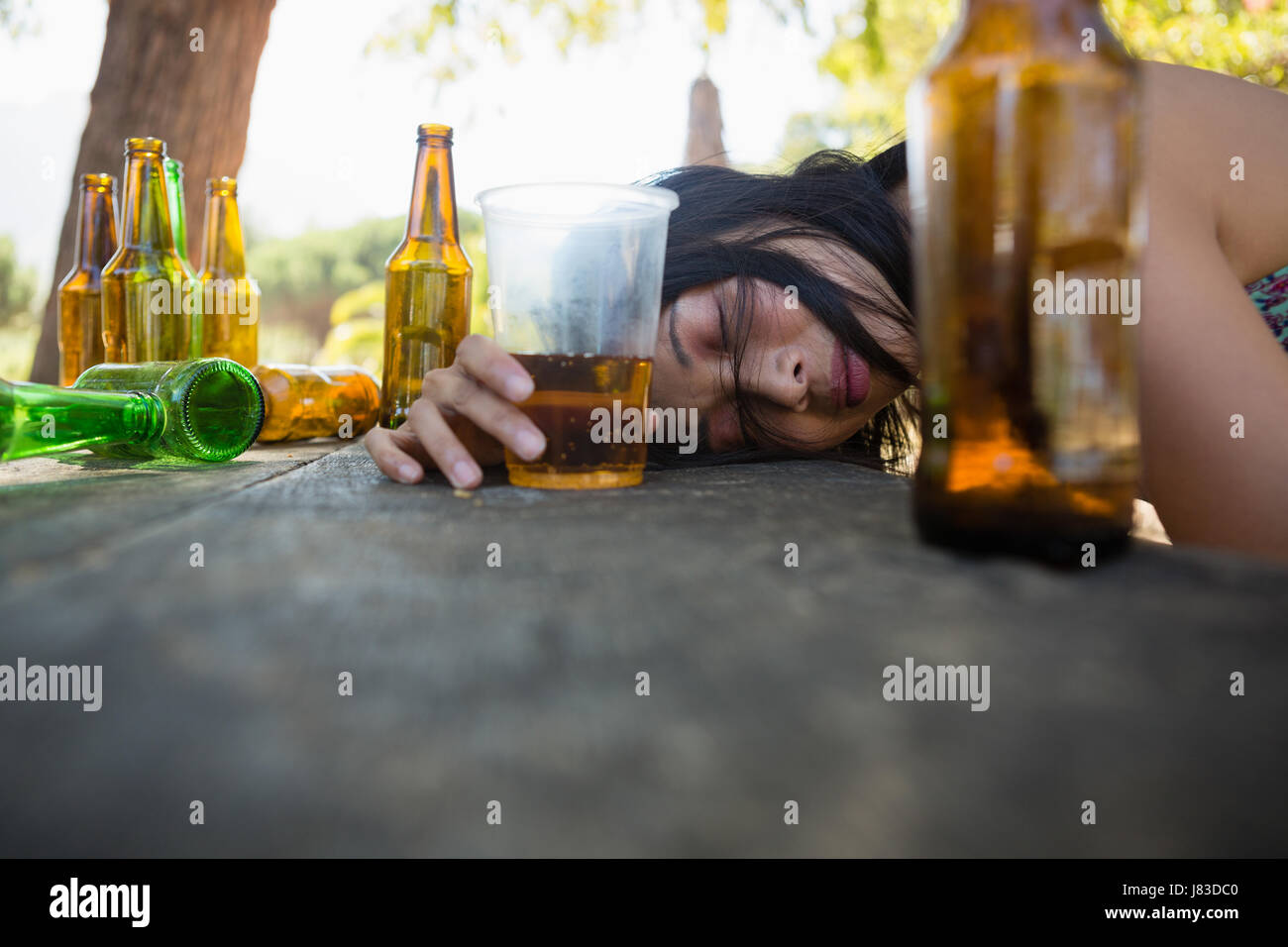 Drunken woman sleeping on the table and holding a glass of beer in the