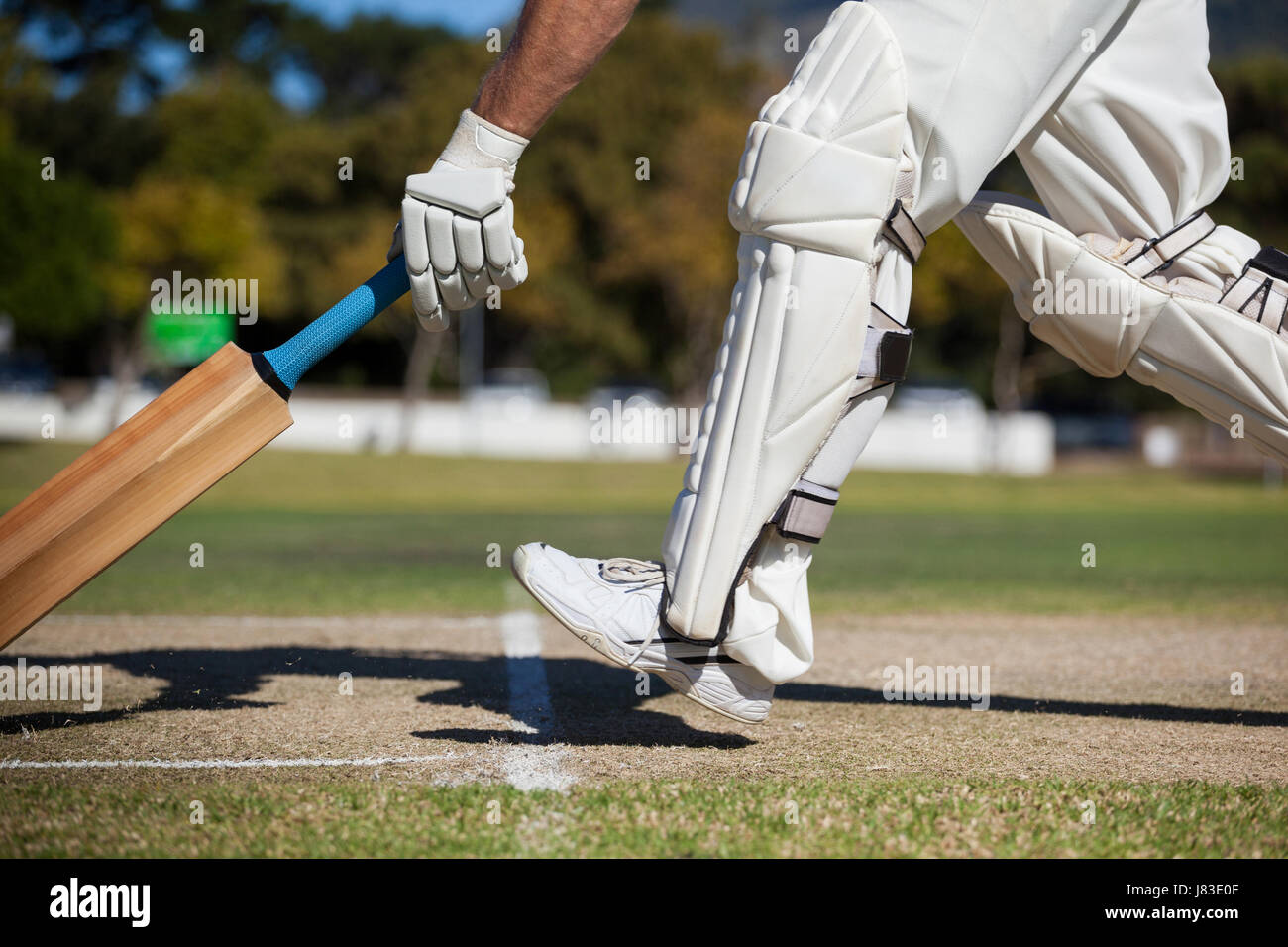 Low section of cricket player scoring run on field during sunny day Stock Photo