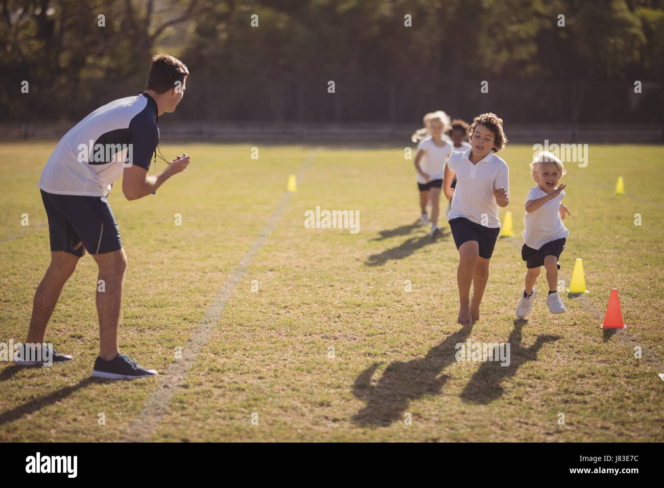 Coach monitoring schoolgirls during running competition in park Stock Photo