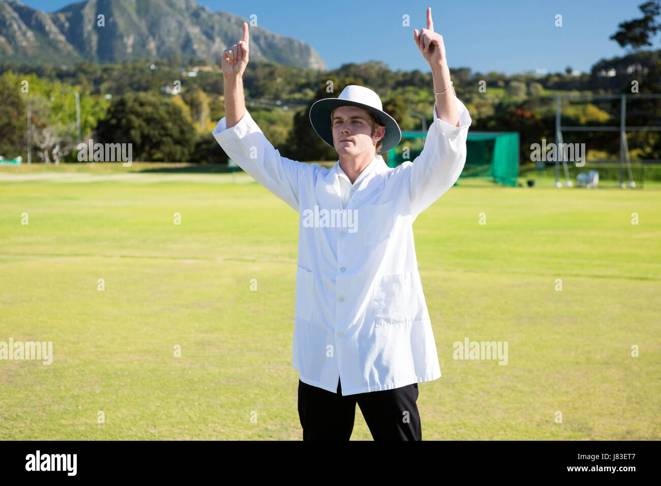 Low angle view of cricket umpire signalling six at match during sunny day Stock Photo