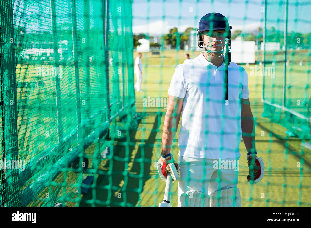 Portrait of confident cricket player wearing helmet standing at pitch