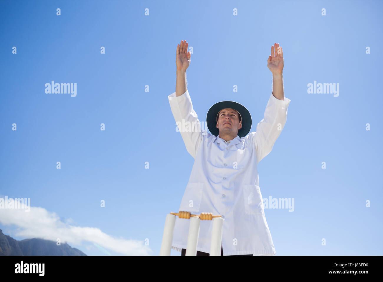 Low angle view of cricket umpire signalling six while standing against sky at match Stock Photo