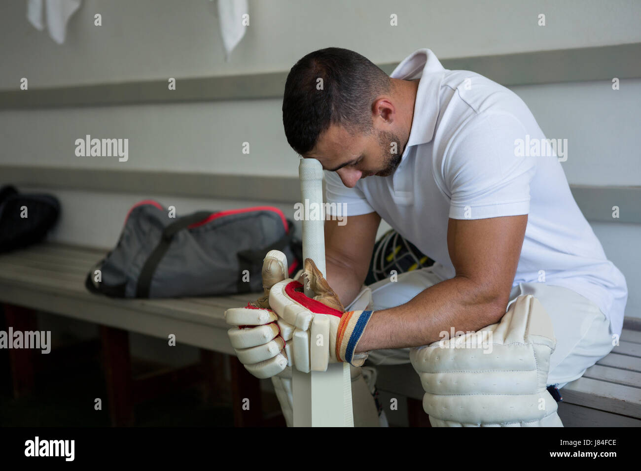 Close up of stressed cricket player sitting on bench at locker room Stock Photo