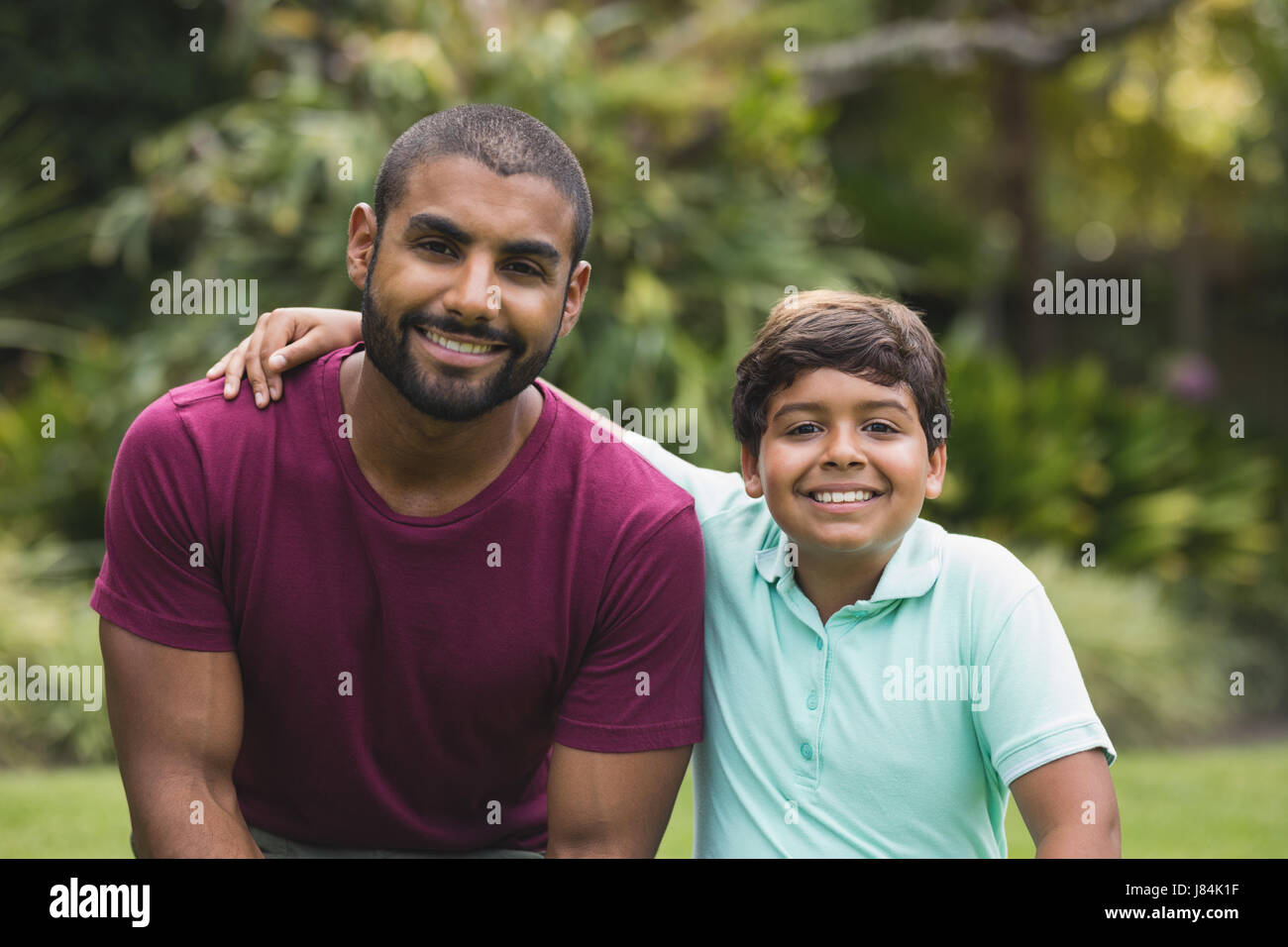 Portrait of smiling father and son sitting at park Stock Photo - Alamy