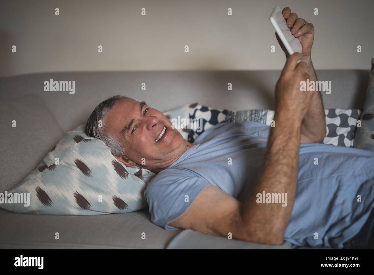 Portrait of smiling senior man holding digital tablet while lying on sofa at home Stock Photo