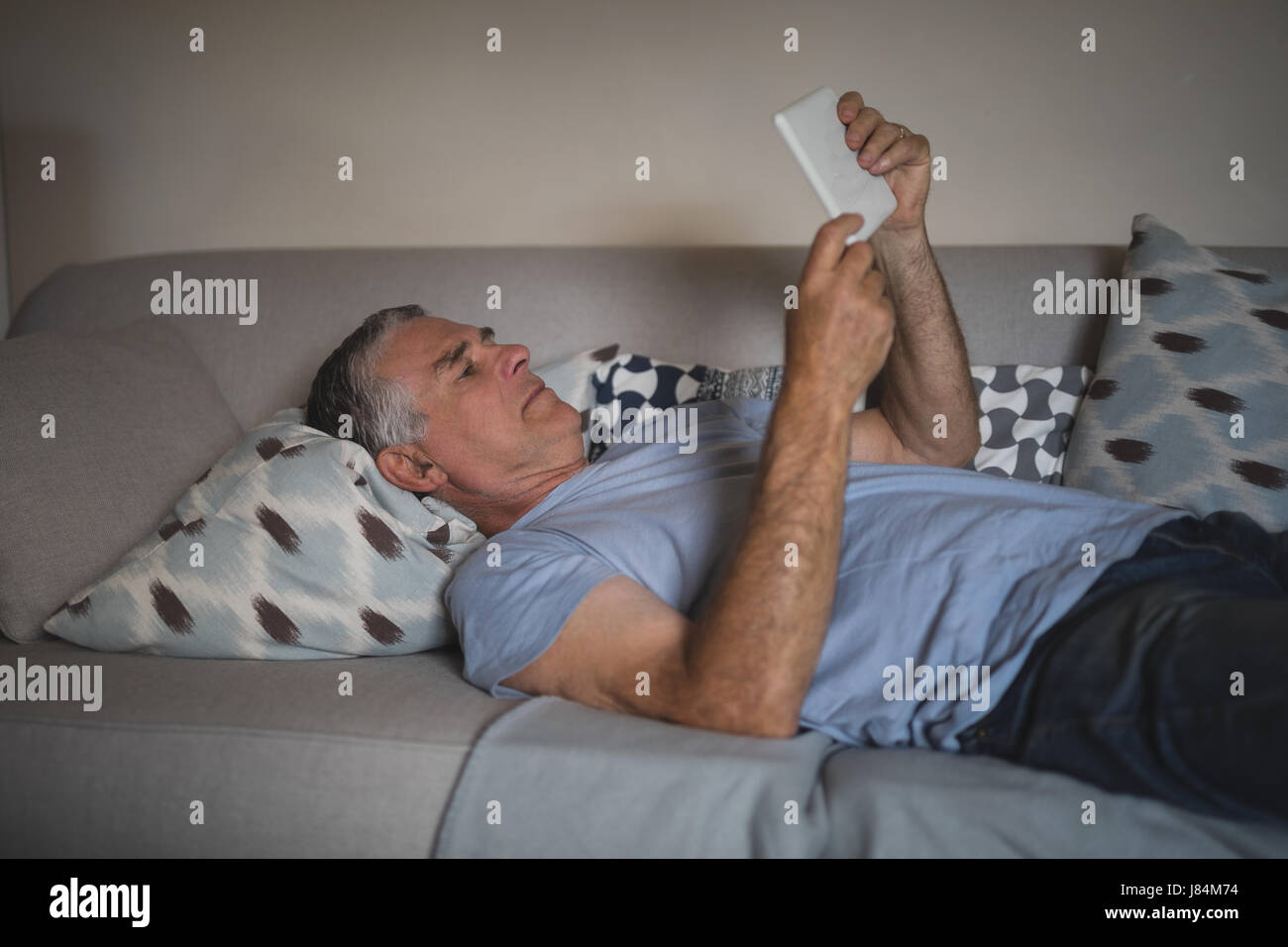 Senior man watching digital tablet while lying on sofa at home Stock Photo