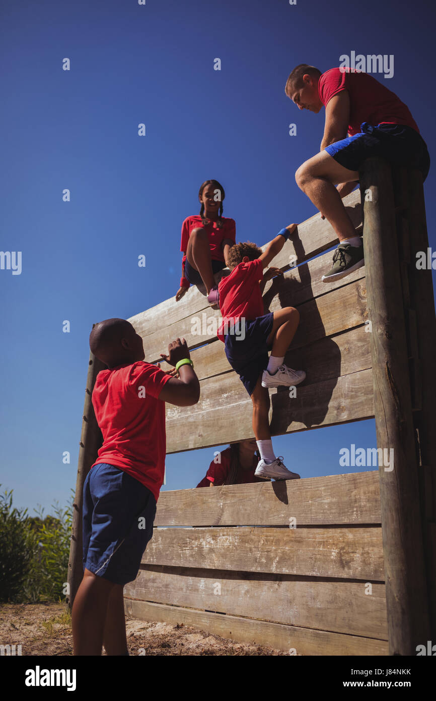 Trainer assisting kids to climb a wooden wall during obstacle course
