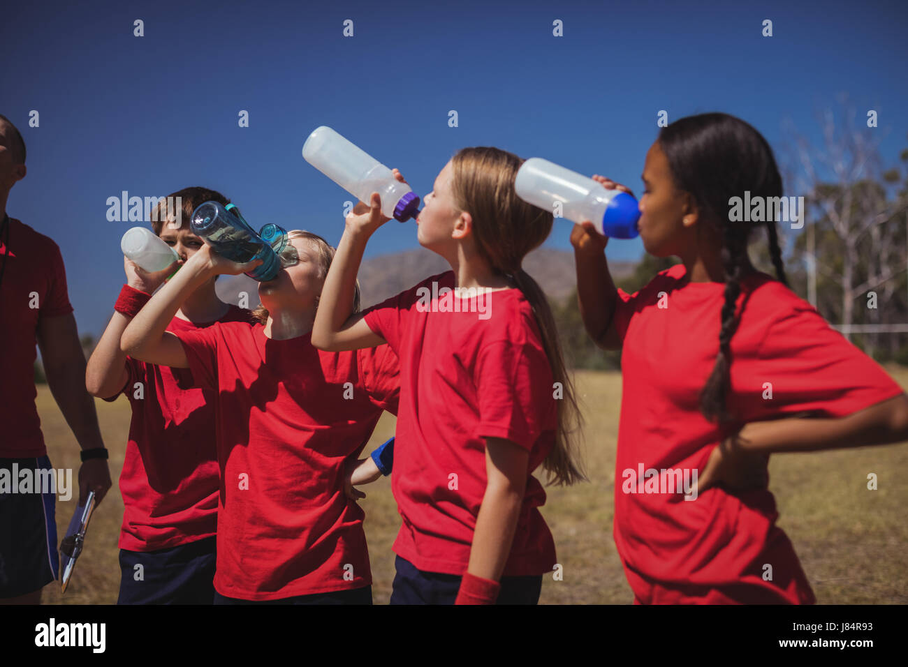 Trainer and kids drinking water in the boot camp on a sunny day Stock