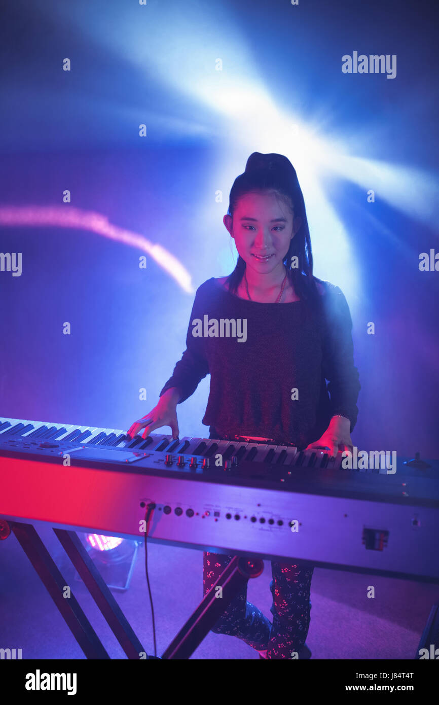 Portrait of smiling female musician playing piano in illuminated nightclub Stock Photo