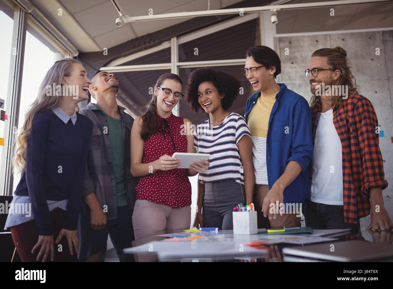 Confident businesswoman using digital tablet while discussing idea with cheerful team in creative office Stock Photo
