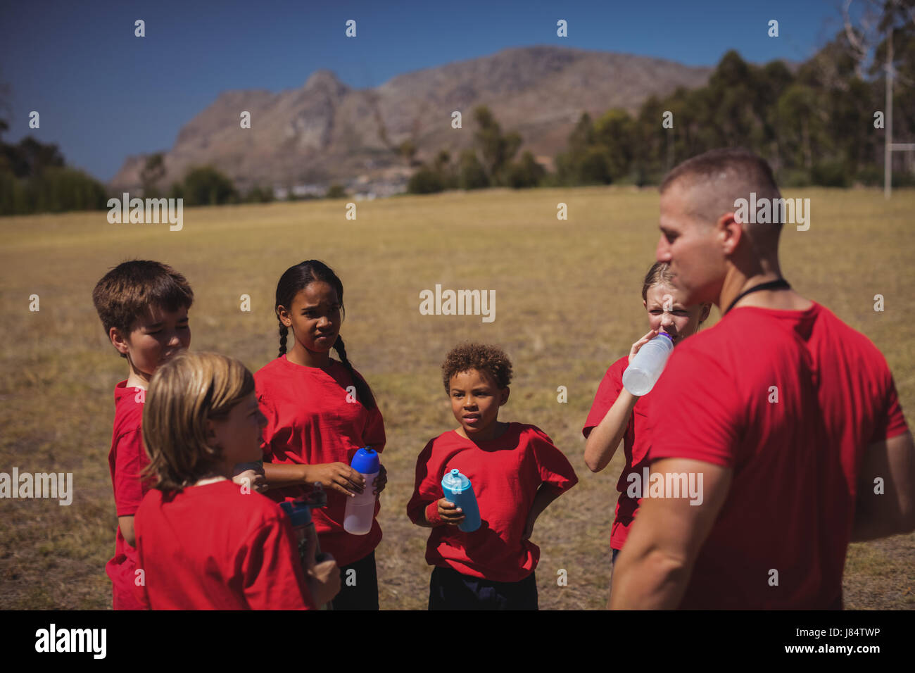 Trainer and kids drinking water in the boot camp on a sunny day Stock