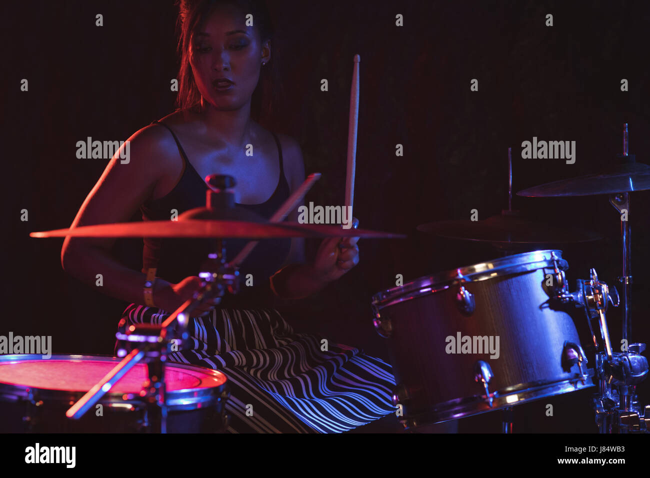 Confident female drummer playing drum kit in nightclub Stock Photo
