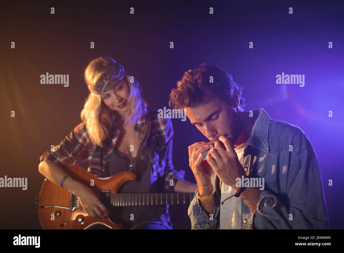 Female guitarist looking at male musician playing harmonica in music concert Stock Photo Alamy