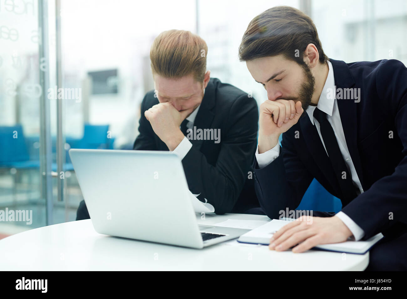 Stressed businessmen sitting by workplace in front of laptop Stock Photo