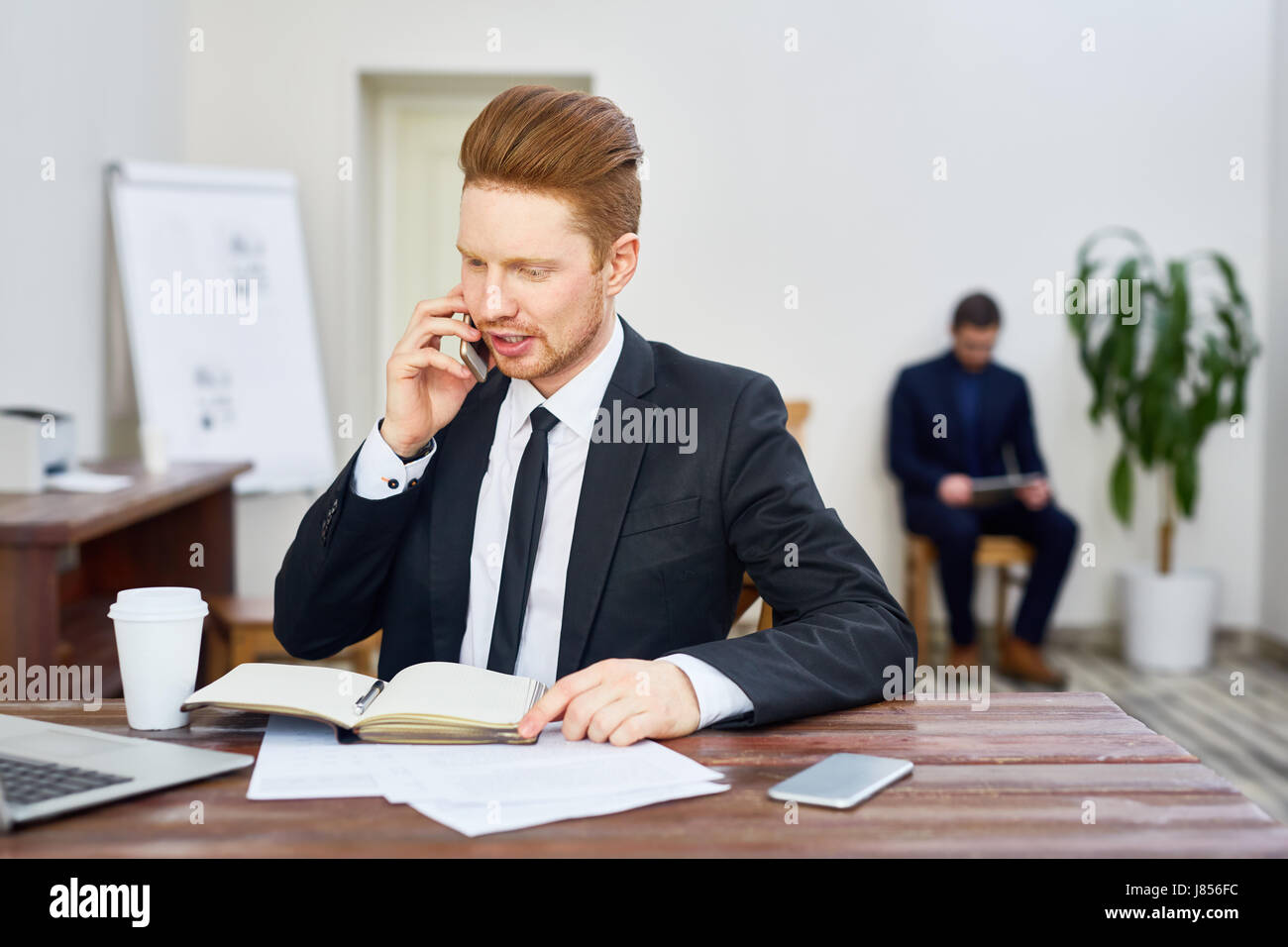 Portrait of young red haired man in business suit working in office answering phone calls Stock Photo