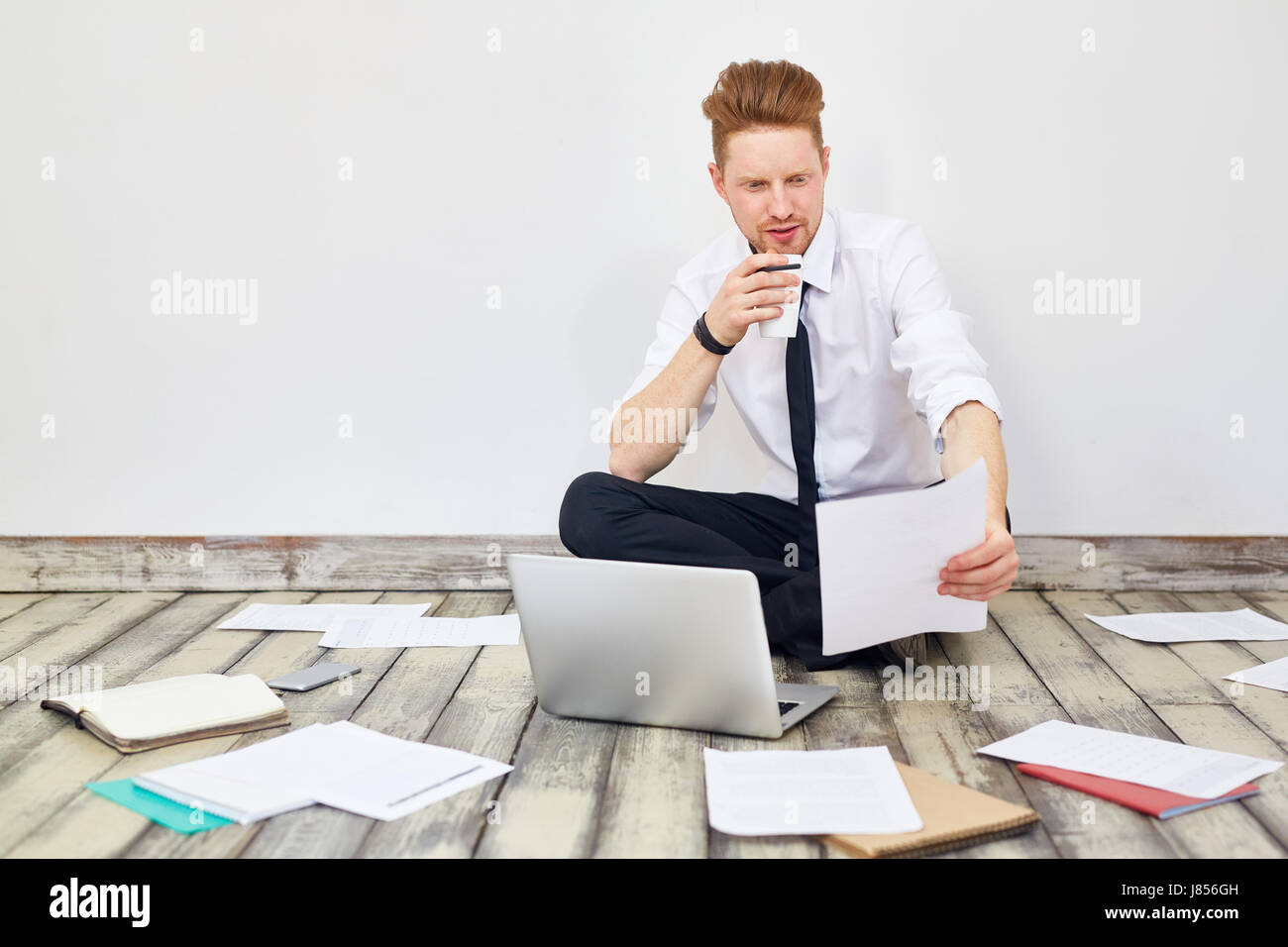 Portrait of modern young businessman sitting cross legged on floor in ...
