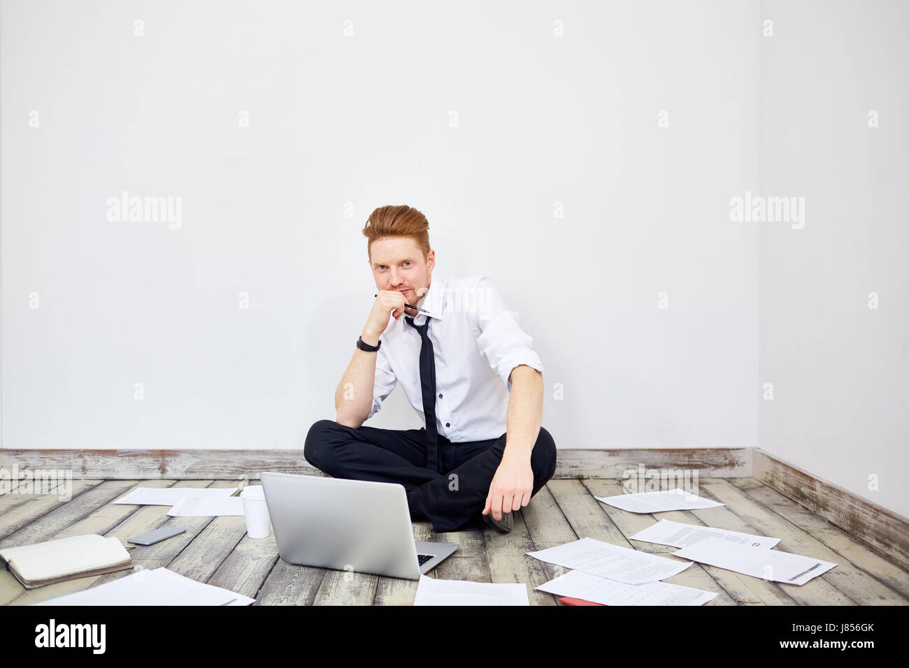 Portrait of modern young businessman sitting cross legged on floor in ...