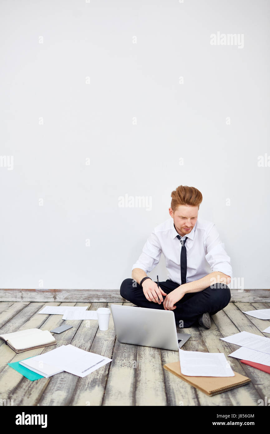 Portrait of modern young businessman sitting cross legged on floor in ...