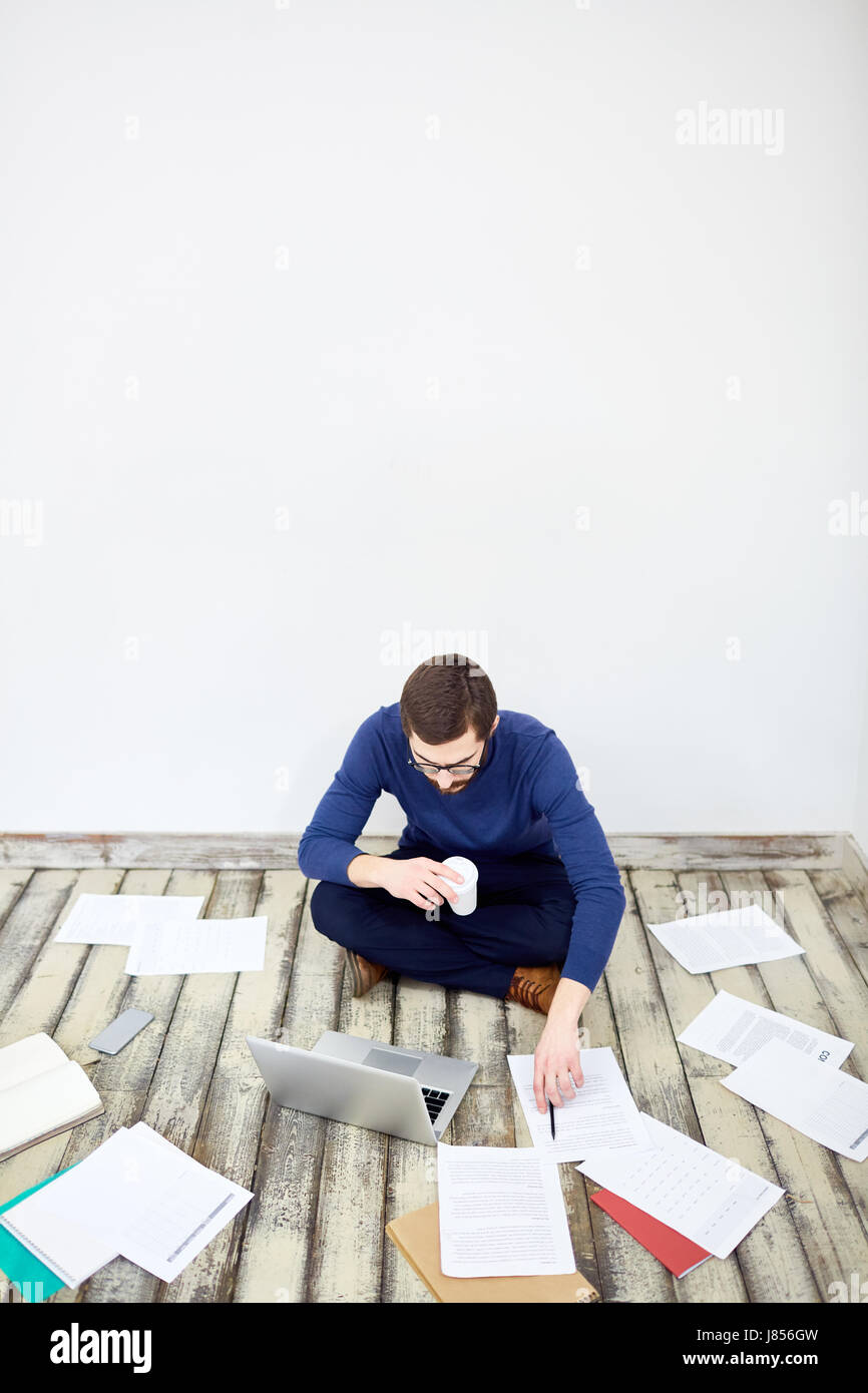 Portrait of modern freelancer sitting cross legged on floor in office ...