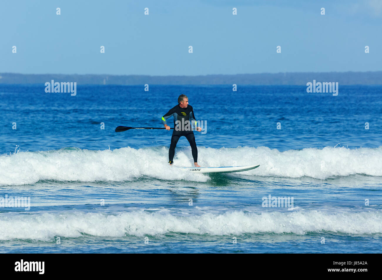 Man 50-60 surfing on a stand up paddleboard and wearing a wetsuit, 7 Mile Beach, Gerroa, New South Wales, NSW, Australia Stock Photo