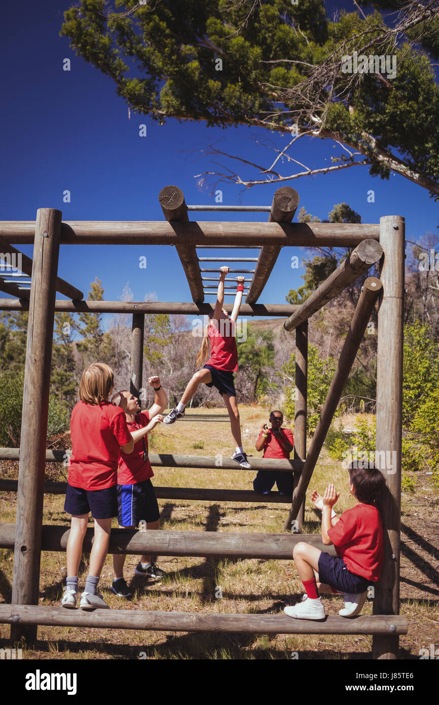 Trainer assisting girl to climb monkey bars during obstacle course training in the boot camp Stock Photo