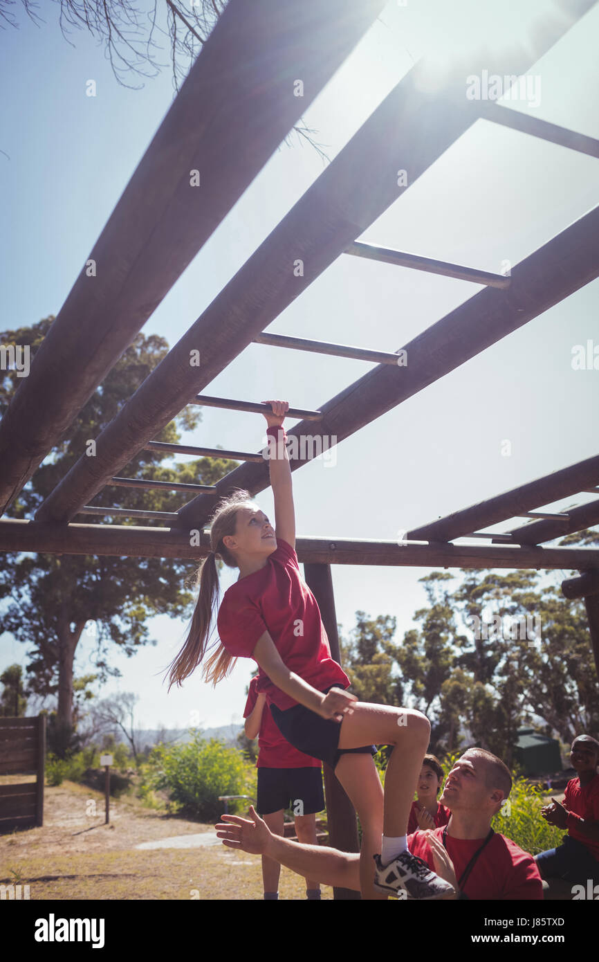 Trainer assisting kids to climb monkey bars during obstacle course training at boot camp Stock Photo