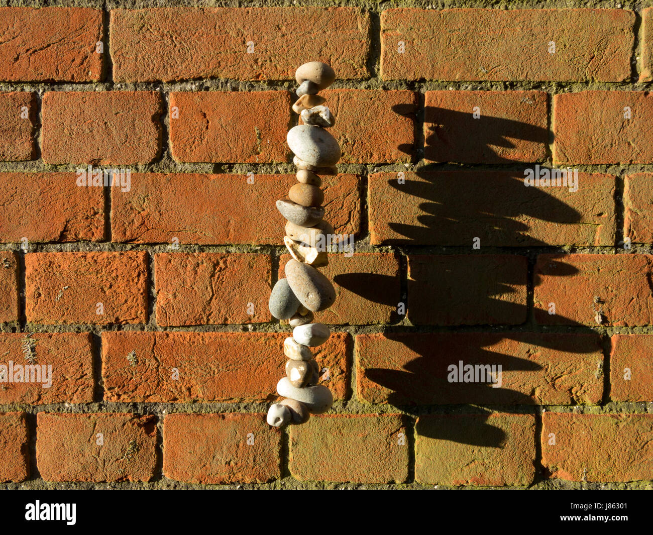 Stacked pebbles in a column seeming to levitate in mid-air with shadow against a redbrick wall Stock Photo