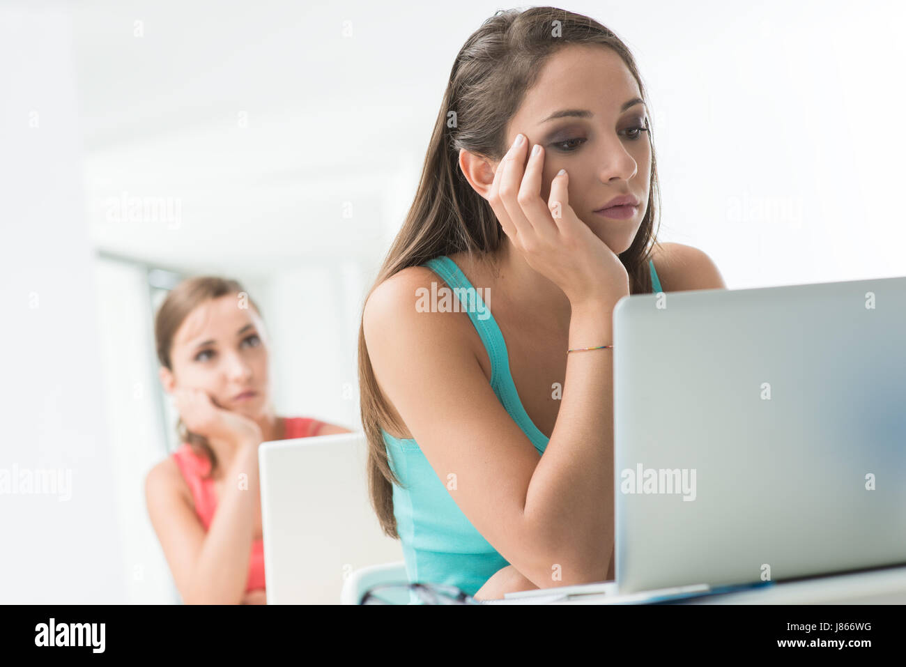 Bored tired girl sitting at school desk with hand on chin and using a ...