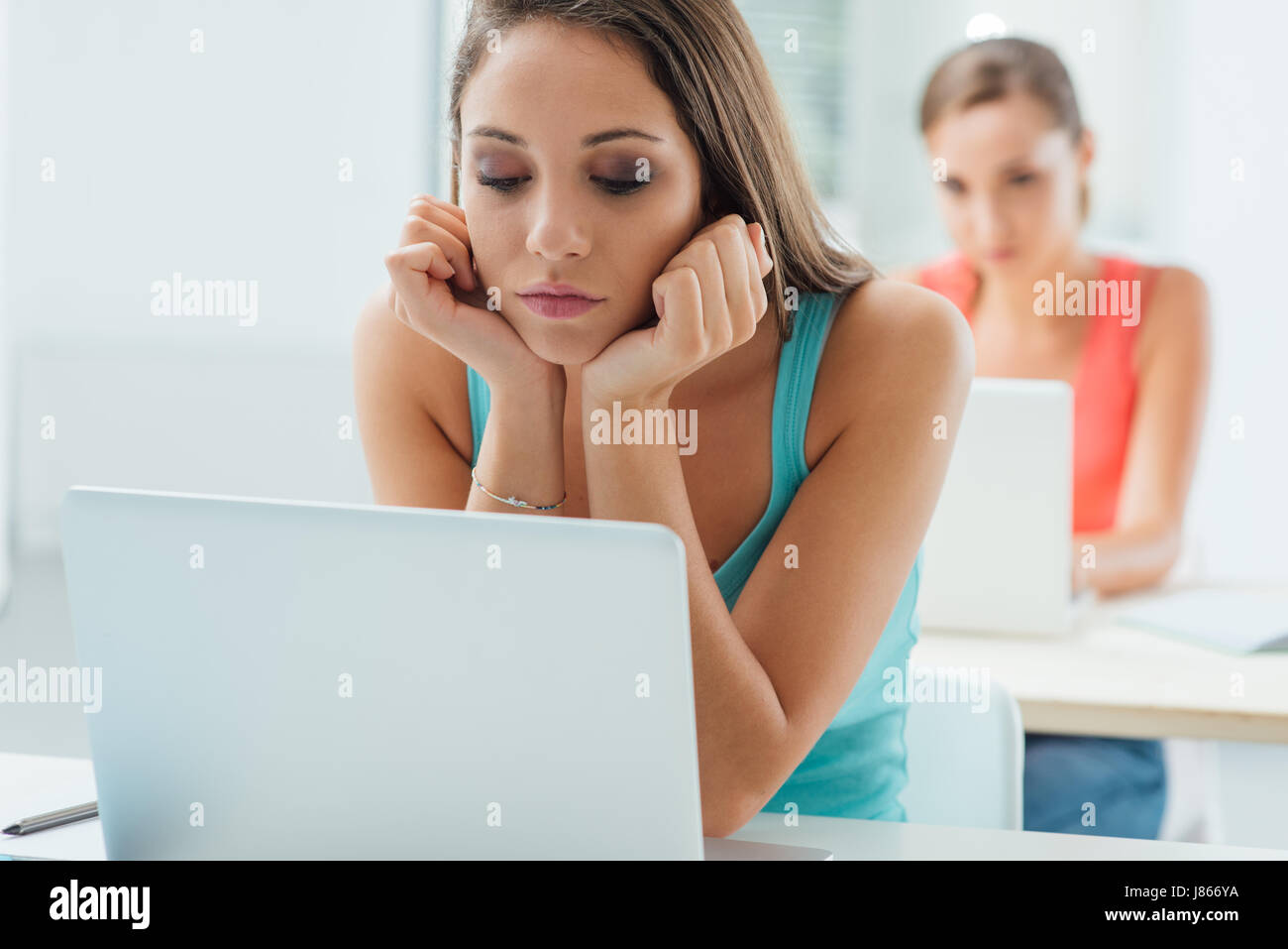 Bored tired girl sitting at school desk with hand on chin and using a ...