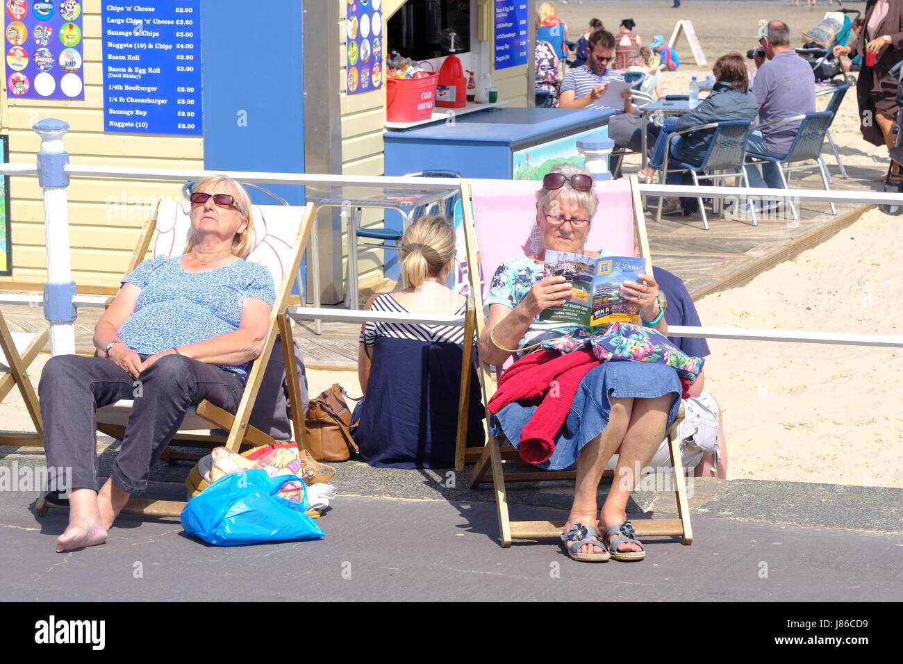 Weymouth, Dorset, UK. 27 March 2017.  Two women sit in deckchairs  on Weymouth seafront as the temperature rises during the afternoon on the Dorset coast. Credit: Tom Corban/Alamy Live News Stock Photo