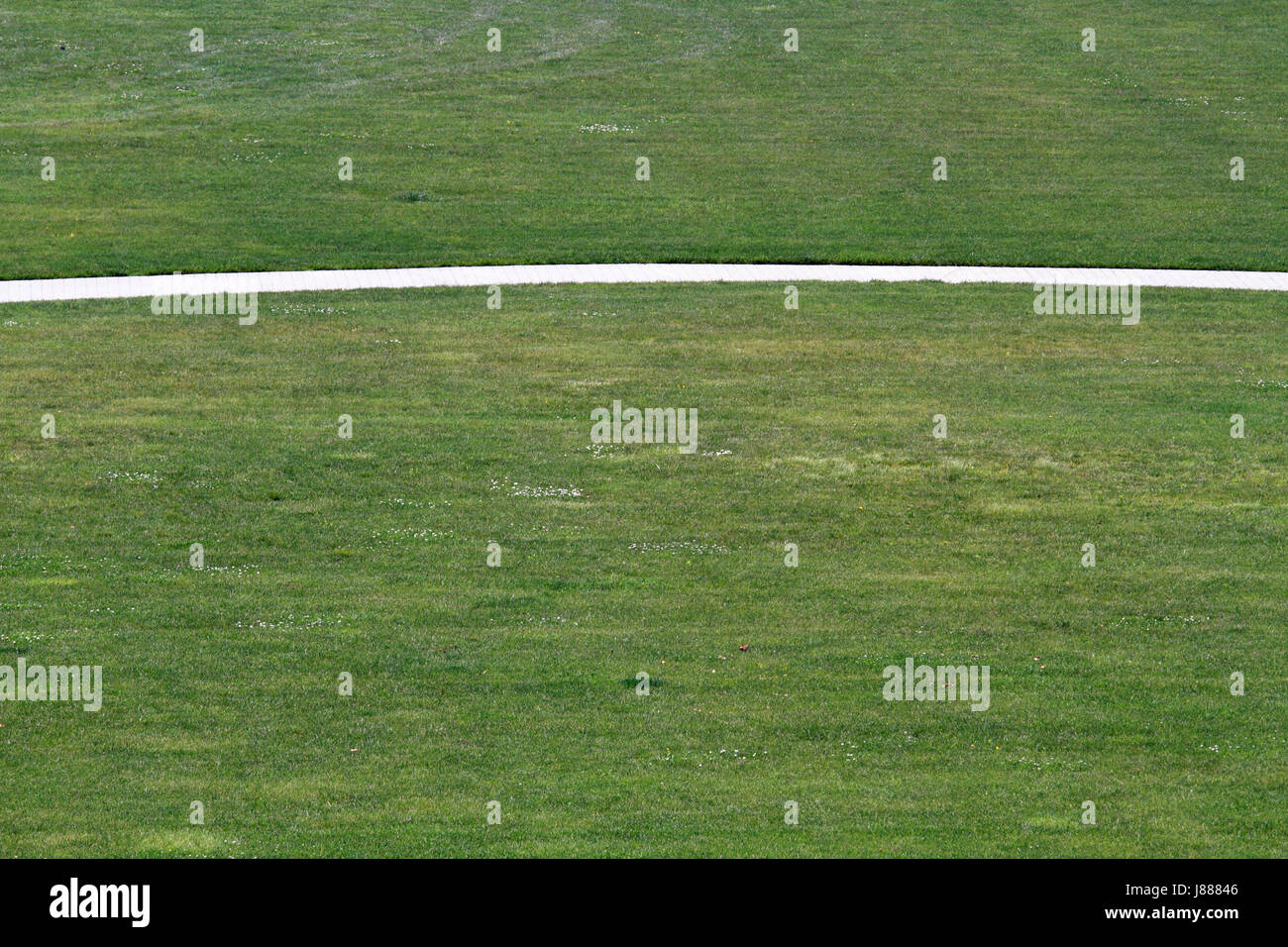 A sidewalk arcing through a grassy field Stock Photo