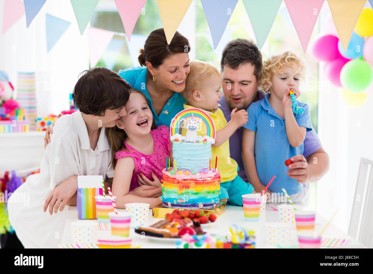 Kids birthday party with unicorn rainbow cake for little girl. Family