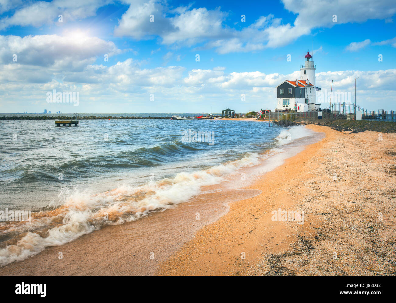 Beautiful lighthouse on the sea coast and blue sky with clouds at sunset in spring in Netherlands. Landscape with yellow sand, sea and beacon. Marine  Stock Photo