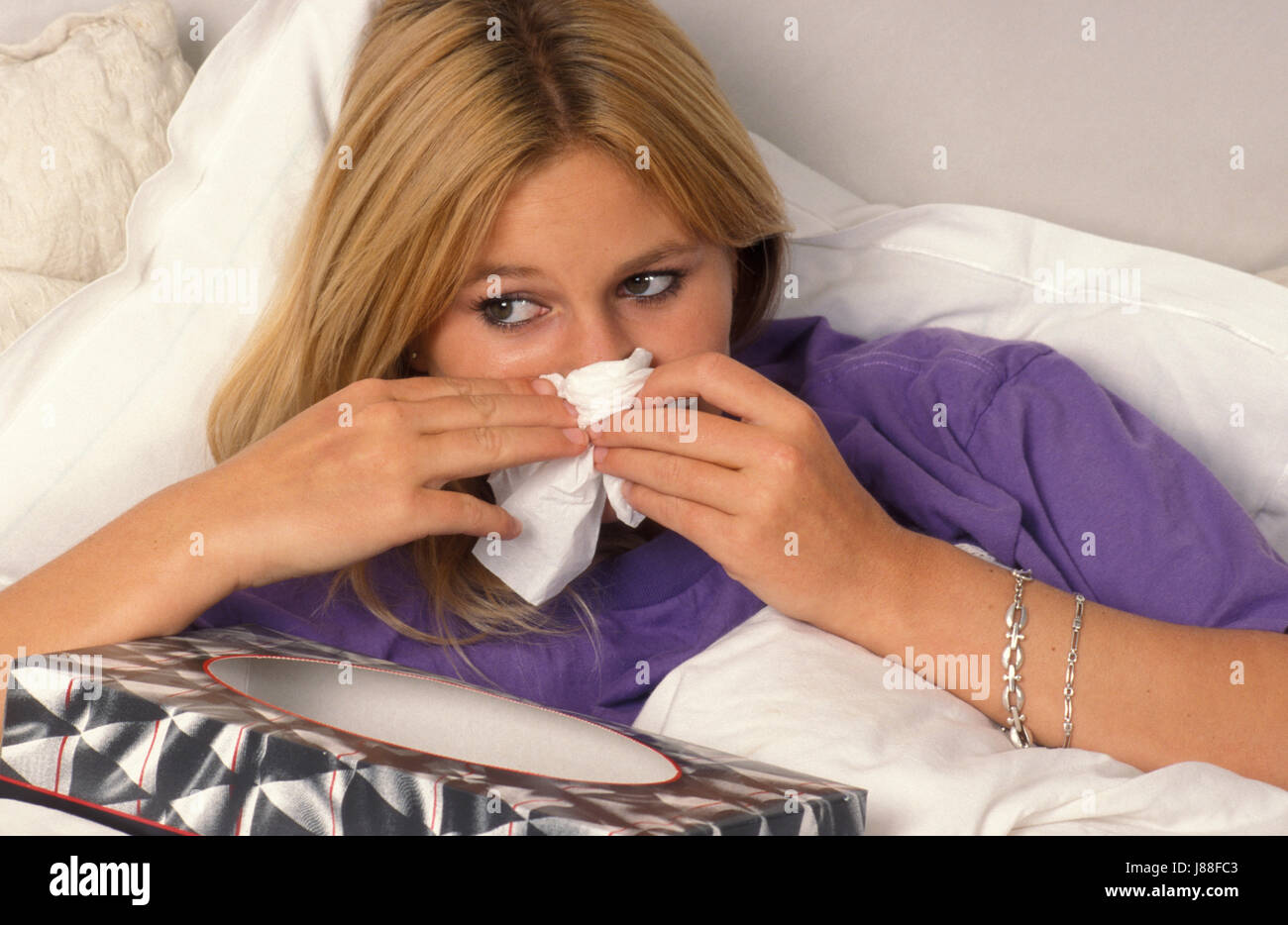 young woman in bed blowing her nose on tissue Stock Photo