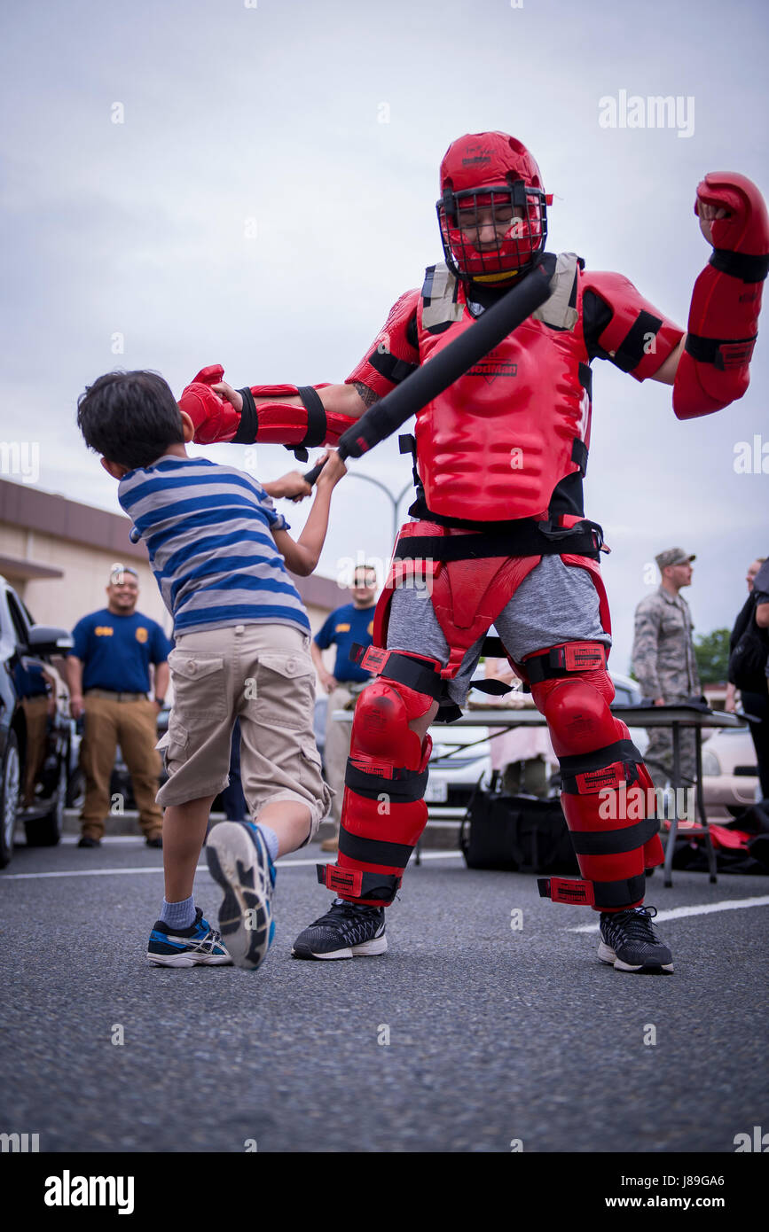 A child hits a 374th Security Forces Squadron member in padded training suit during a Police Week event, May 17, 2017, at Yokota Air Base, Japan. The event included displays and demonstrations of various vehicles, weapons and tools used by U.S. and Japanese law enforcement. (U.S. Air Force photo by Airman 1st Class Donald Hudson) Stock Photo