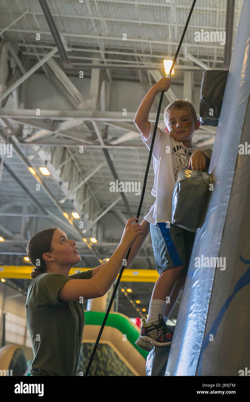 Lance Cpl. Wrenetta Howard assists a child up a rock climbing wall at Kids Corps Day on Marine Corps Air Station New River, May 20, 2017. Kids Corps Day gives children an opportunity to visit their parents’ place of work and lets them interact with one another. Howard is a volunteer for Kids Corps Day. (U.S. Marine Corps photo by Lance Cpl. Juan Madrigal) Stock Photo