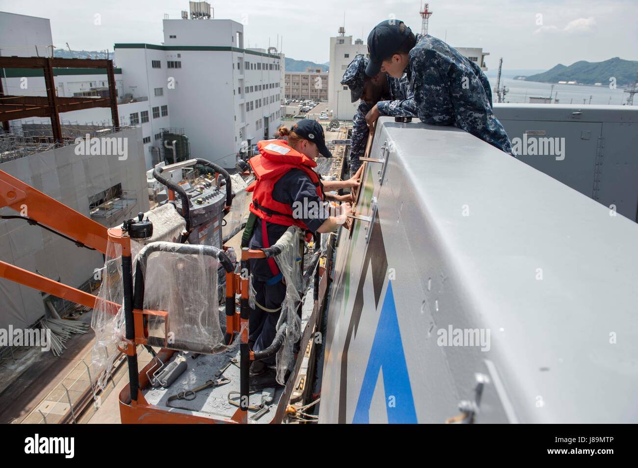 170523-N-ZL062-012 SASEBO, Japan (May 23, 2017) Sailors aboard the amphibious transport dock USS Green Bay (LPD 20) paint the Battle Effectiveness 'E' Award on the ship’s port bridgewing. Green Bay is forward-deployed to Sasebo, Japan, serving forward to provide a rapid-response capability in the event of a regional contingency or natural disaster. (U.S. Navy photo by Mass Communication Specialist Seaman Sarah Myers/Released) Stock Photo