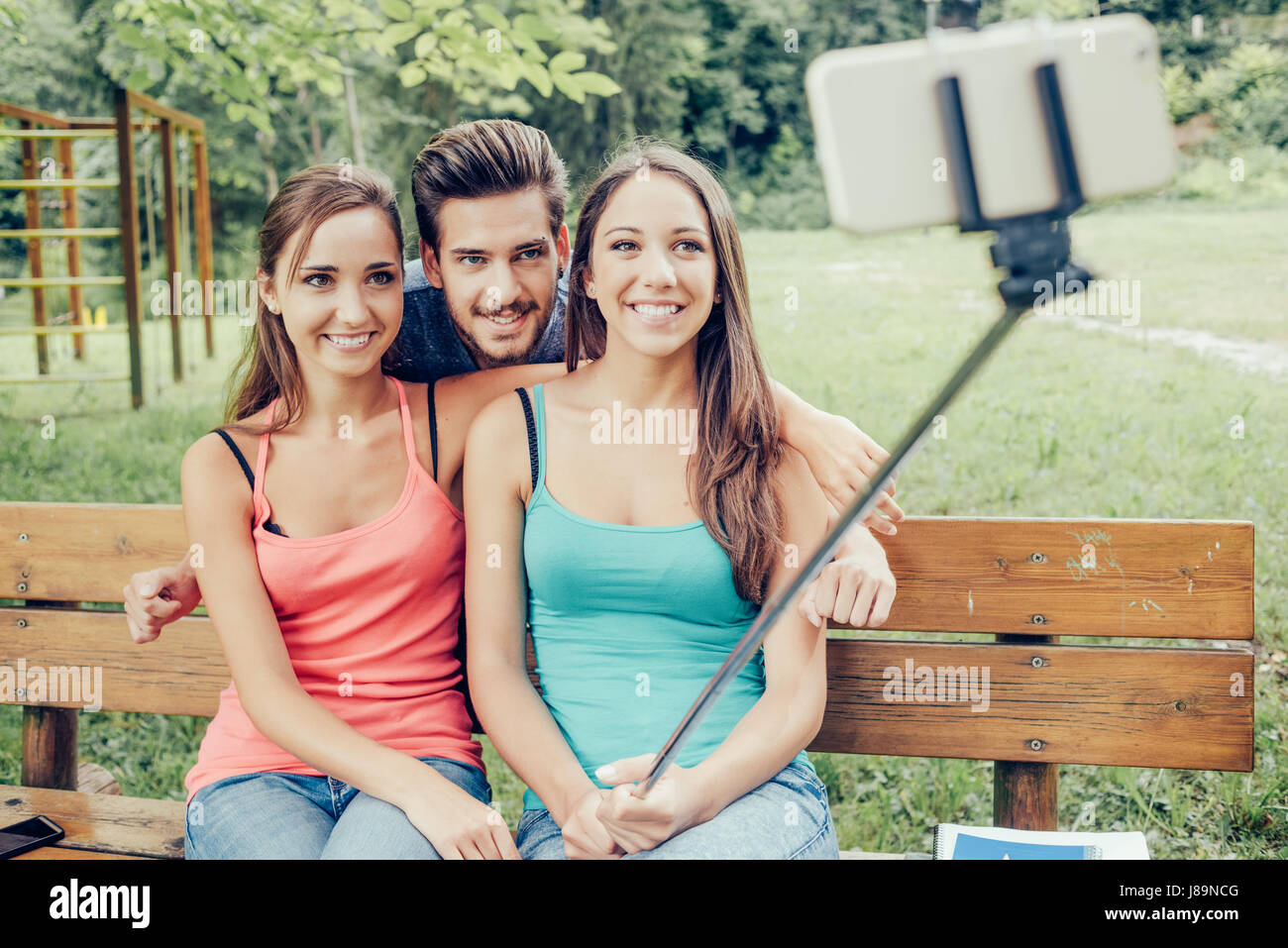 Cheerful smiling teenagers relaxing at the park and taking selfies using a selfie stick Stock Photo