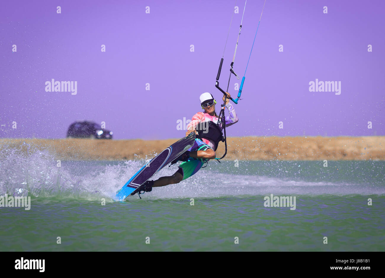Kite surfer rides ideal flat water of the lake lagoon with kite flying in sky making slide trick. Recreation activity and active extreme water sports Stock Photo