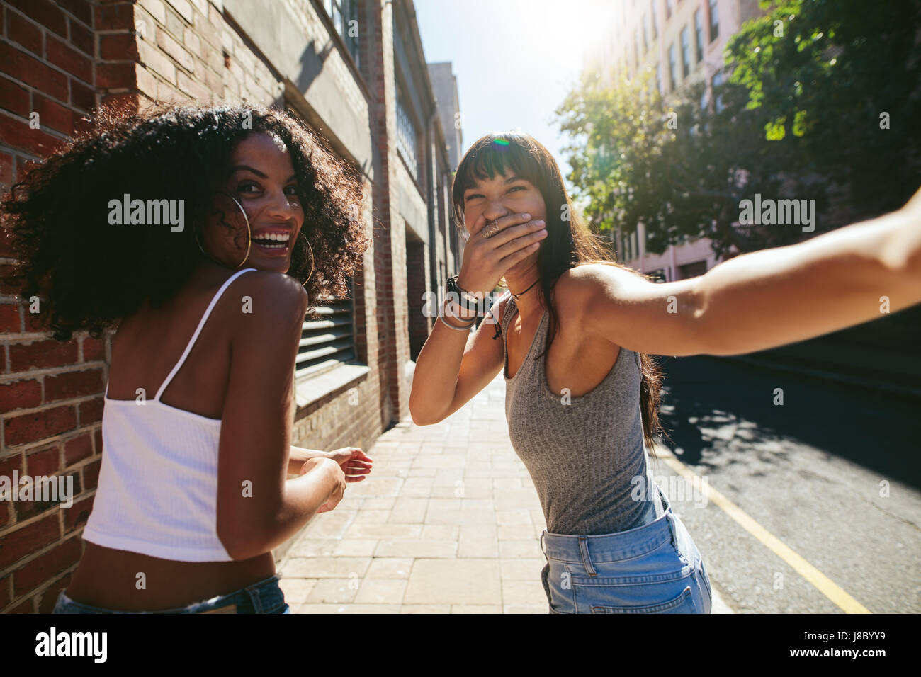 Shot from behind of two young women walking on city street. Female friends walking together outdoors and having fun. Stock Photo