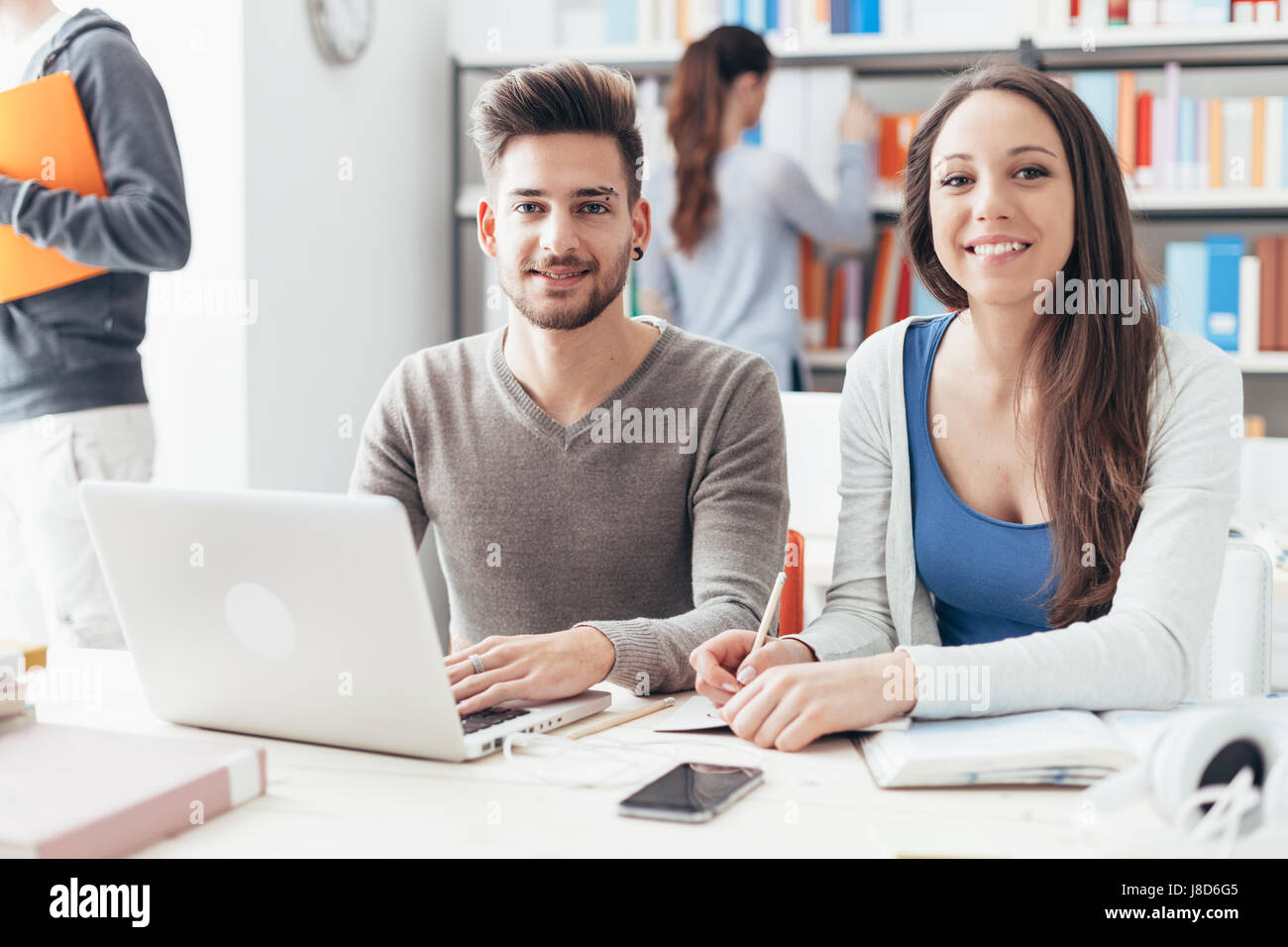 Smiling College Students Sitting At Desk And Studying Together