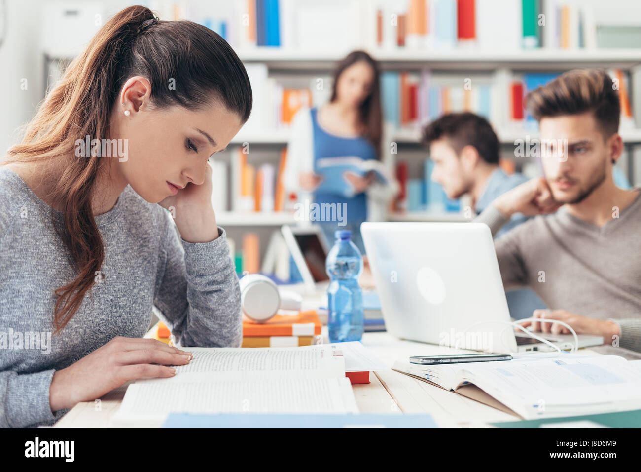 College Students Sitting At Desk And Studying Together Using