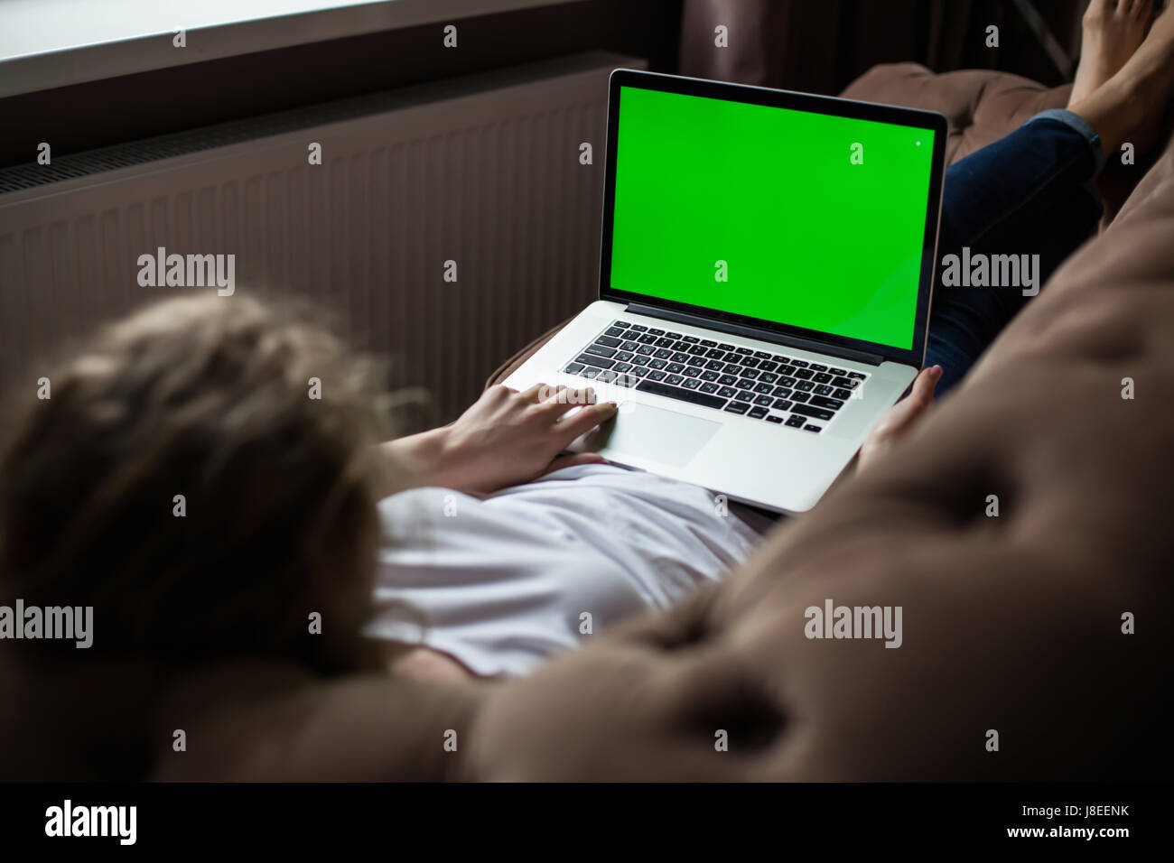 Girl using laptop with green screen. Woman lying on the sofa. Stock Photo