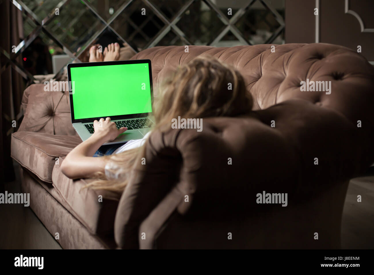 Blonde lying on the sofa with the laptop. Green screen. Stock Photo